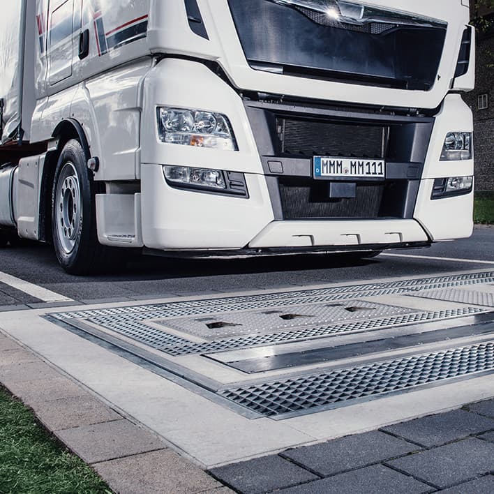 White truck driving over ground-mounted sensor of drive over reader