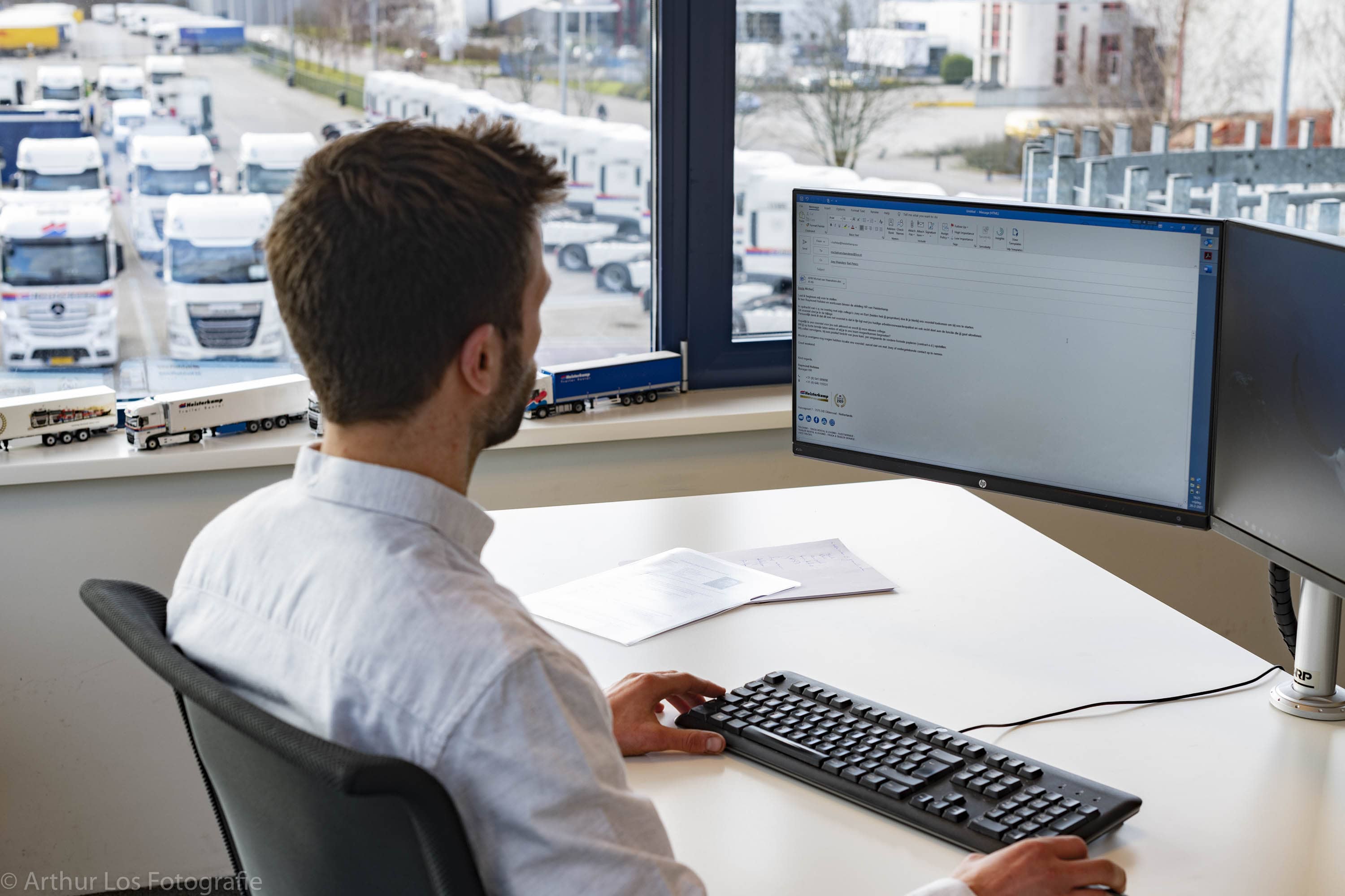 fleet manager looking at FleetOnlineSolutions on-screen with truck fleet in the background